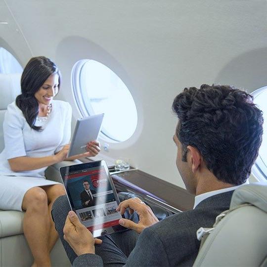 Professional man and woman sit across from each other on a private plane looking at inflight entertainment on their tablets